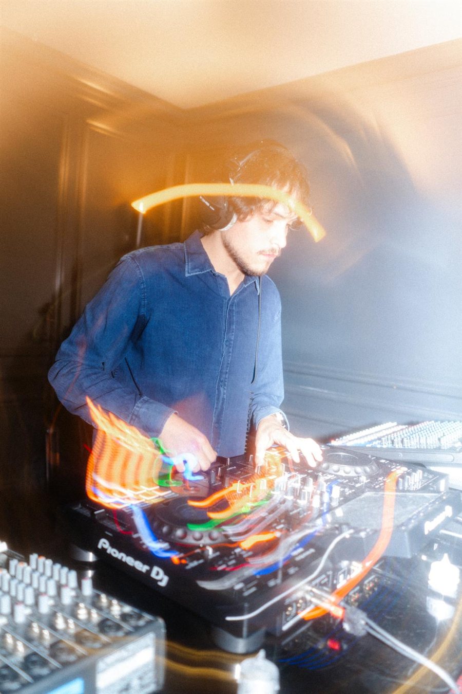 Diego Ramirez DJing on a Pioneer setup, a long exposure catching light trails across the mixer.